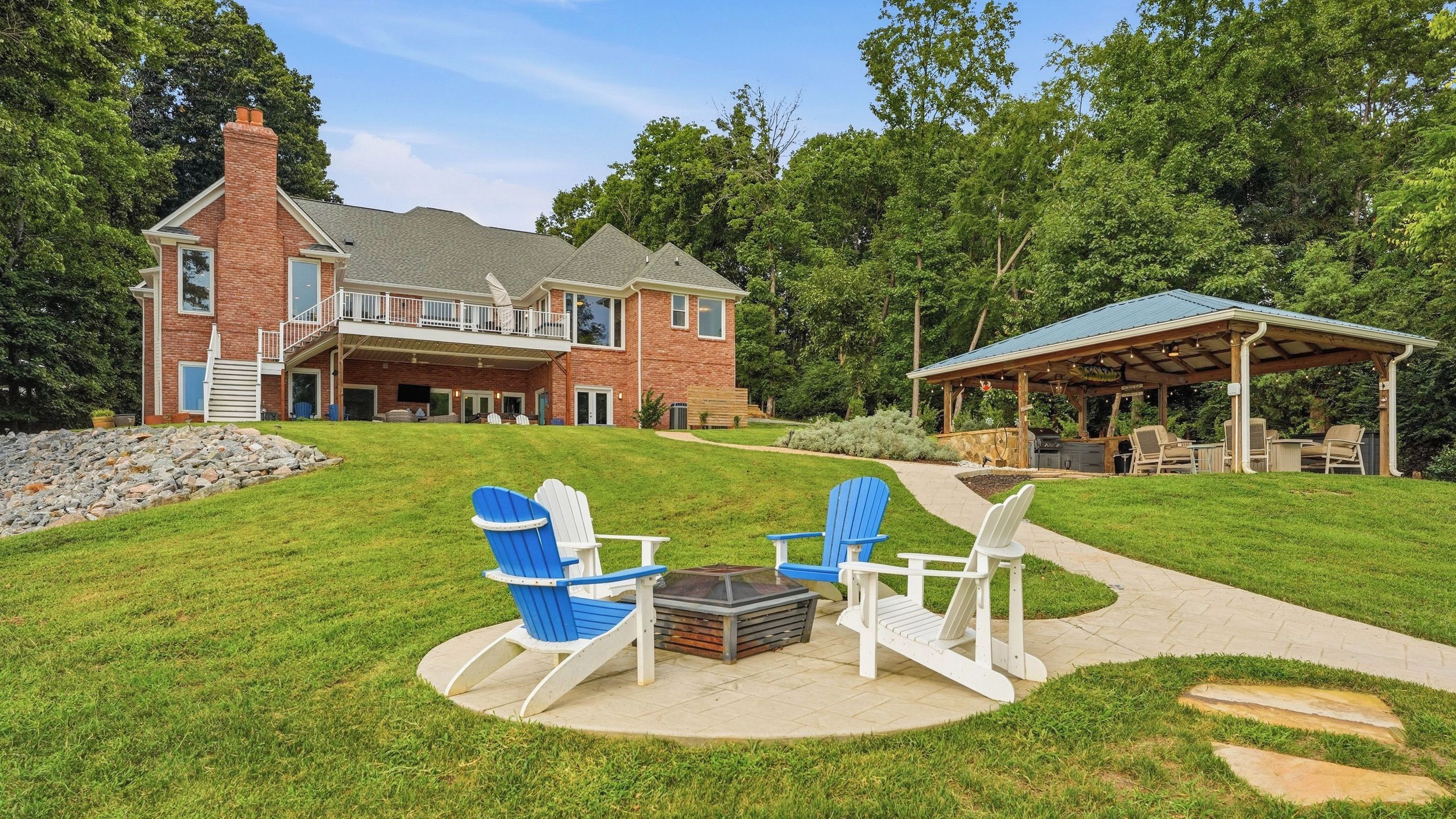 Een tweelaags huis met een terras, Adirondack-stoelen en een vuurkuil.