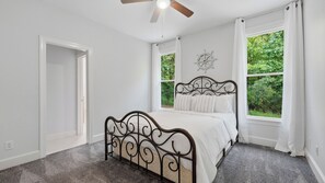 Ein Schlafzimmer mit einem Bett, einem Deckenventilator und Blick auf Grün durch die Fenster.