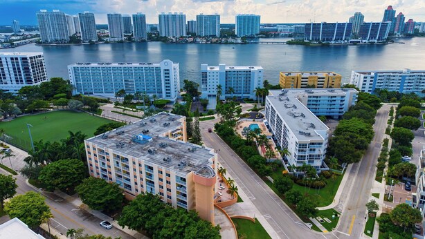 A high-rise hotel with multiple floors, a parking area, and a view of the water and other buildings. - Isle Vista by Avantstay Sunny Isles Condo Shared Pool + Private Balcony Near Beaches (Sunny Isles Beach)