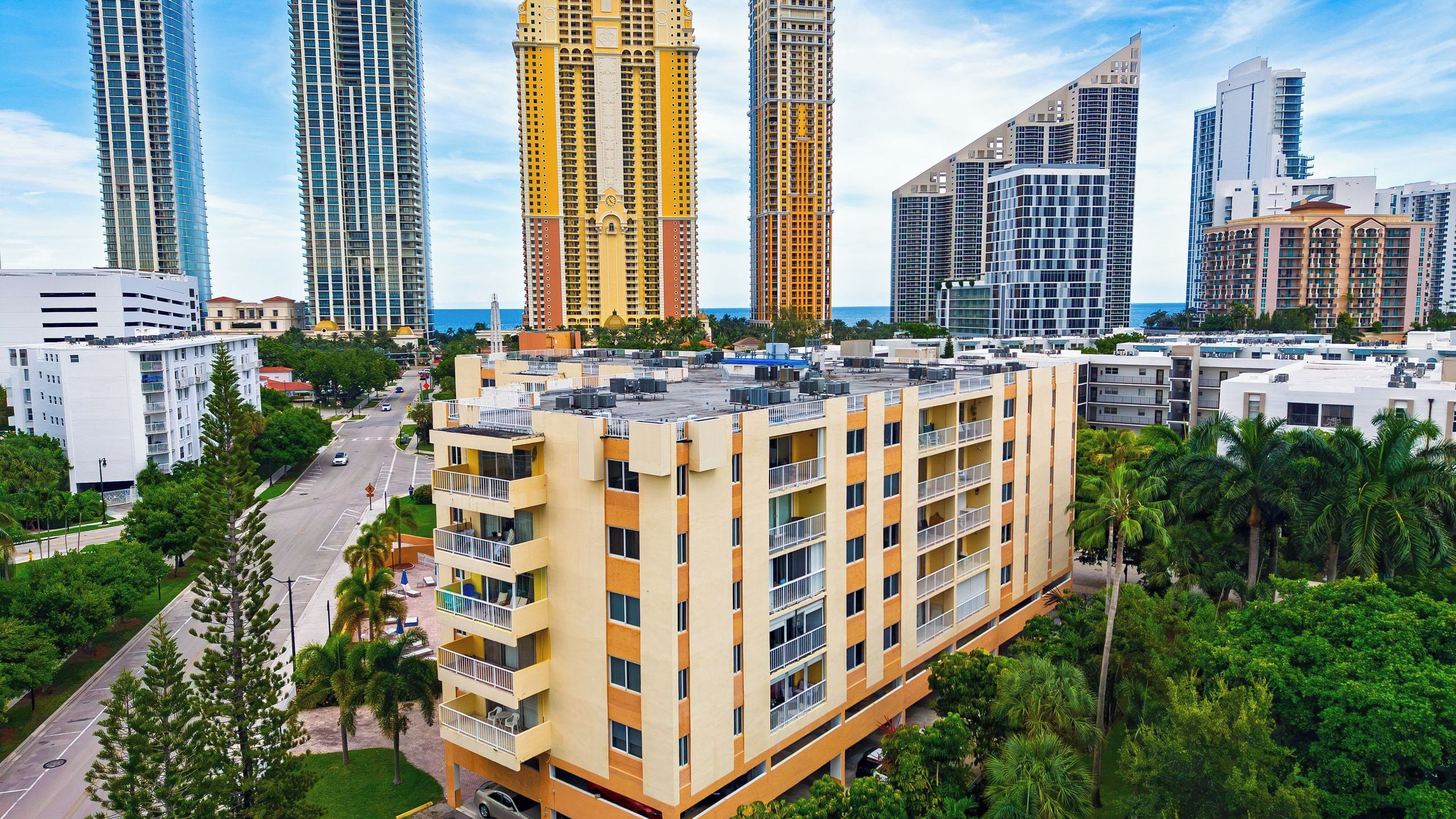 A high-rise building with multiple balconies, surrounded by other tall buildings and palm trees.