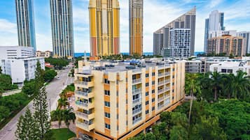 A high-rise building with multiple balconies, surrounded by other tall buildings and palm trees.