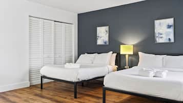 Quarto de hotel com duas camas, piso de madeira, armário branco e duas pinturas abstratas na parede.