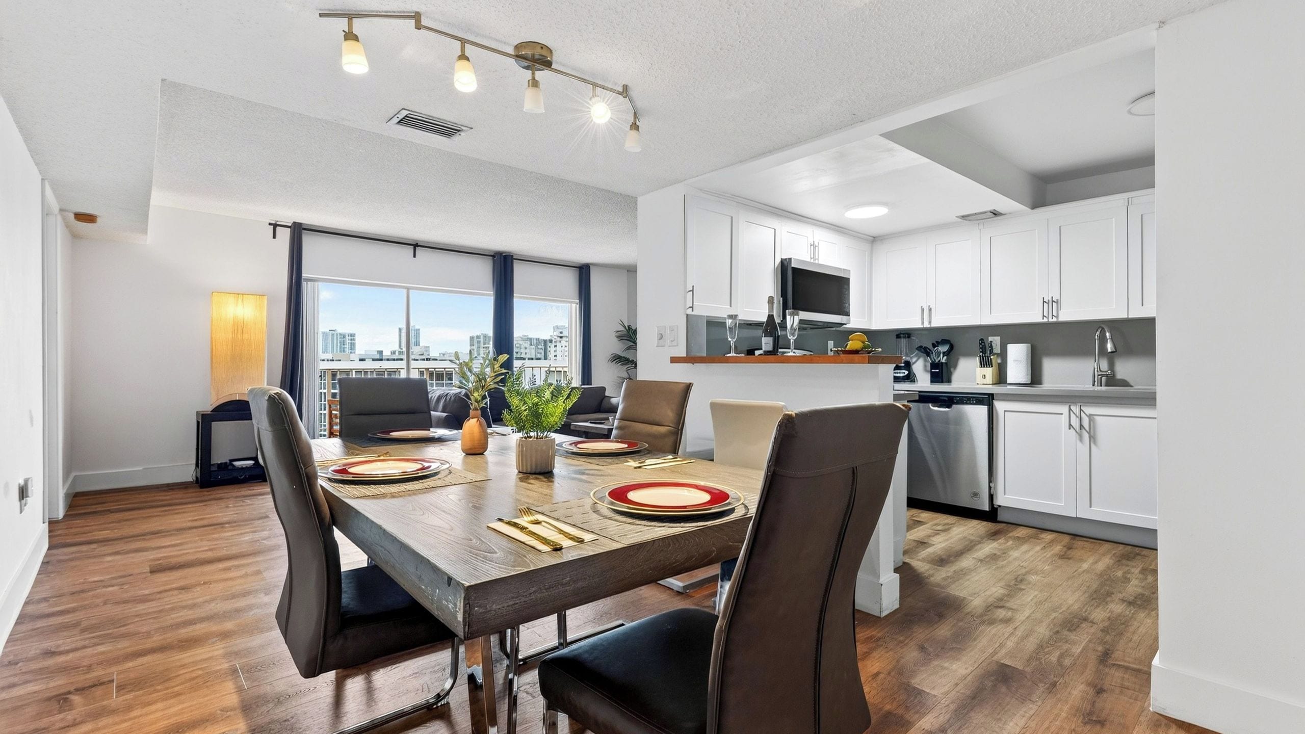 A modern apartment with a dining area, kitchen, and large windows offering a city view.