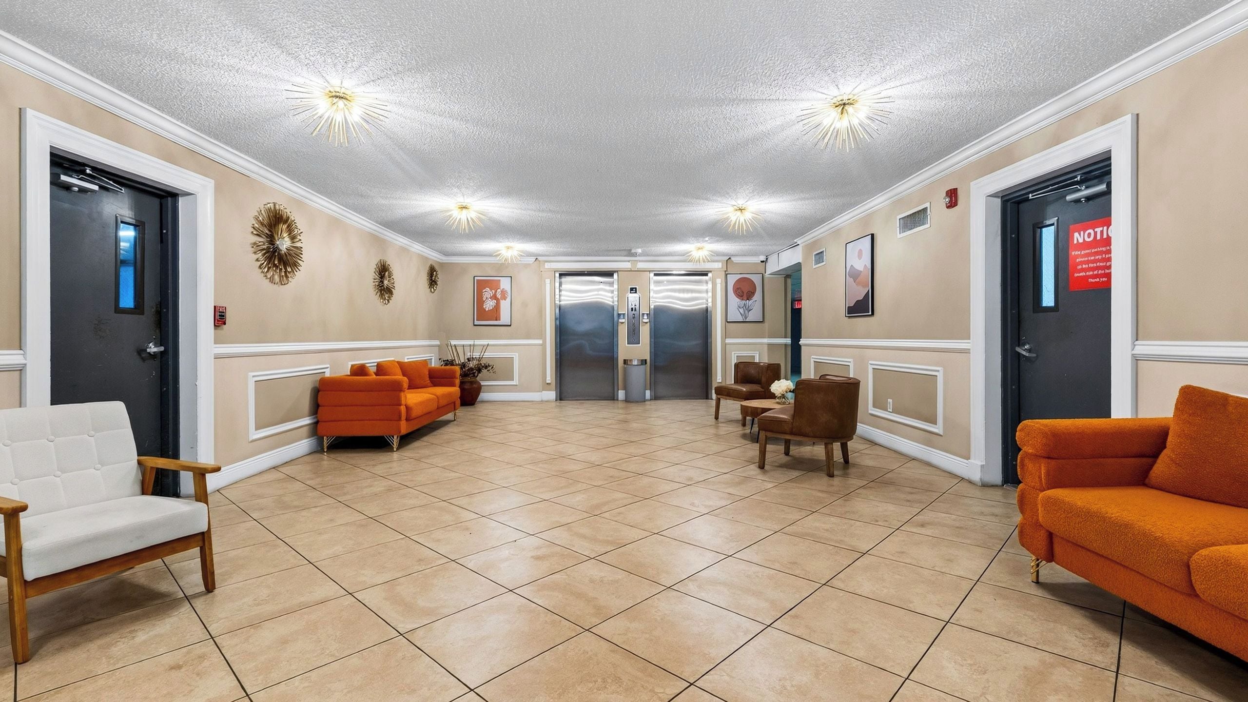 A lobby with a reception desk, two elevators, and seating areas with orange sofas.
