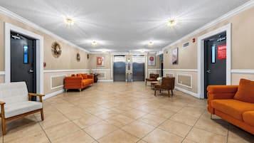 A lobby with a reception desk, two elevators, and seating areas with orange sofas.