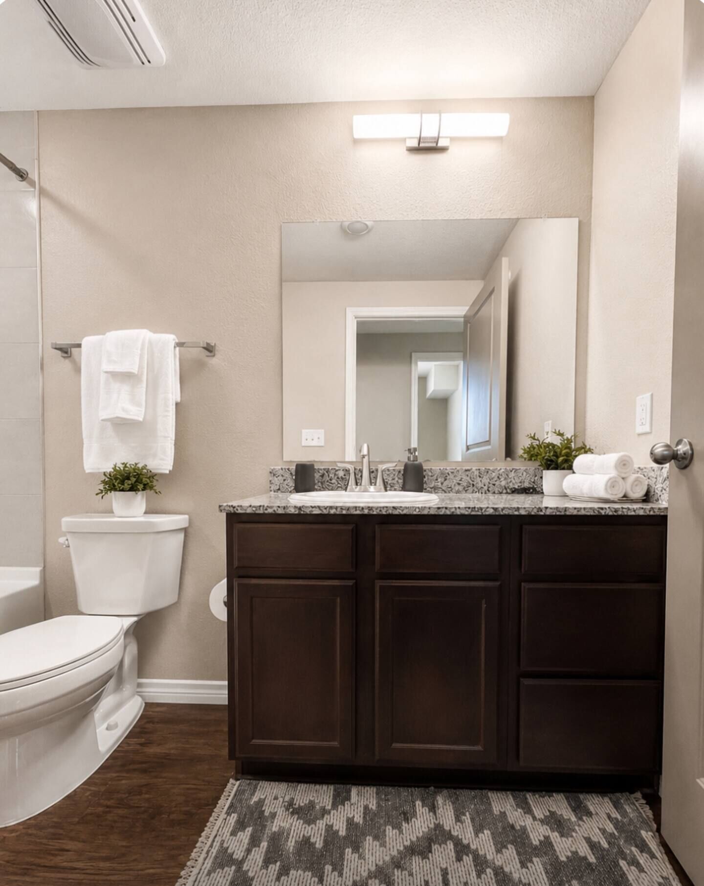 A bathroom with a toilet, a sink with a mirror above it, and a dark wooden cabinet below.