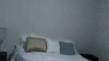 Un lit avec une literie blanche dans une pièce aux murs unis.