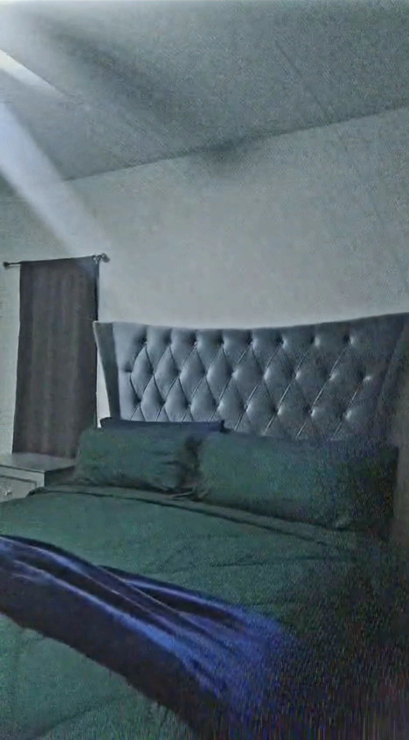 A room with a tufted headboard, a bed with green bedding, and a curtain on the window.