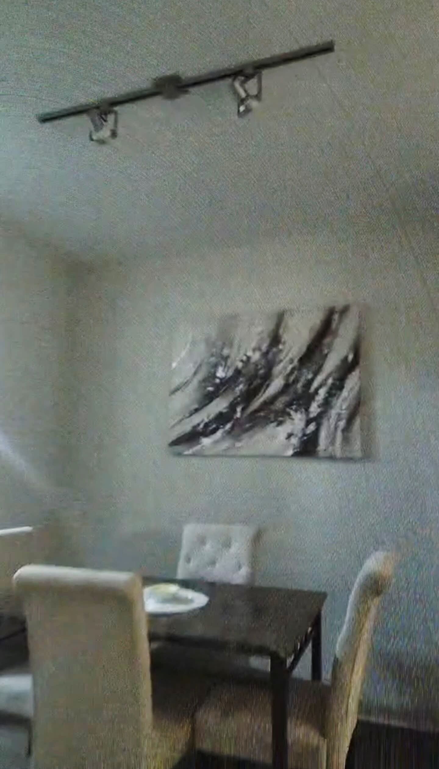 Un espace repas comprenant une table et des chaises, un luminaire fixé au mur et une œuvre d’art abstraite.