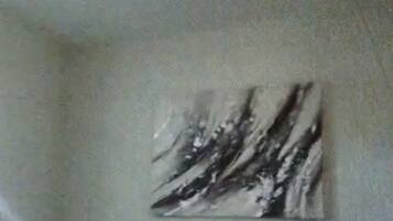 Un espace repas comprenant une table et des chaises, un luminaire fixé au mur et une œuvre d’art abstraite.