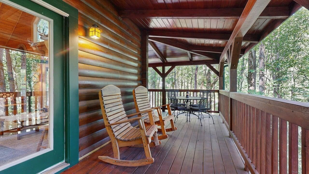 Eine Holzterrasse mit Schaukelstühlen und einem Tisch, mit Blick auf ein bewaldetes Gebiet.