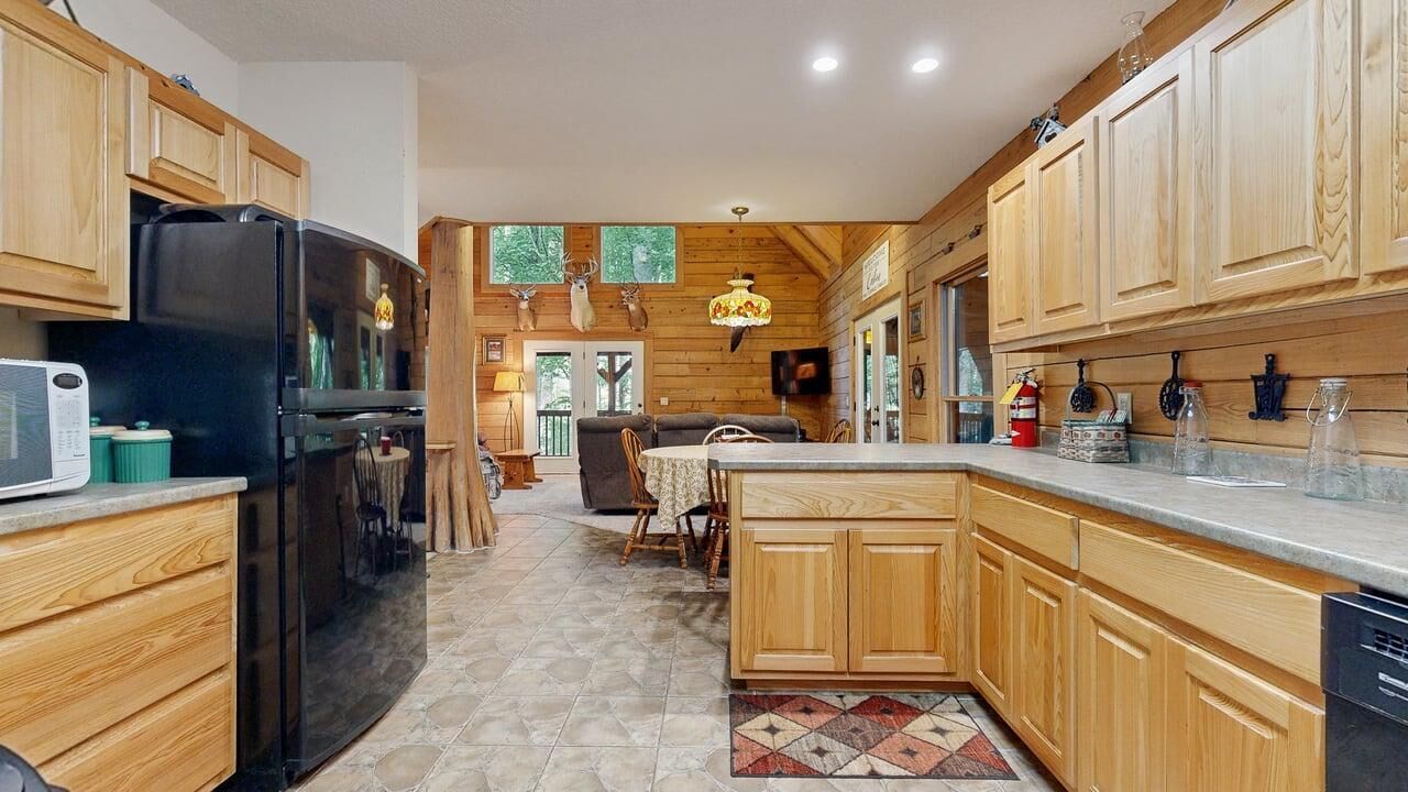 Una cucina con mobili in legno, un frigorifero nero, un'area pranzo con tavolo e sedie, e un tappeto decorato.