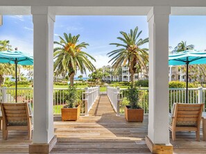 A wooden deck leading to a gated area with palm trees and a view of a building.