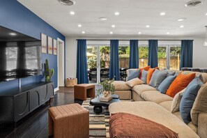 A modern living room with a sectional sofa, a flat-screen TV, and a dining area with outdoor seating. - Heated Pool, Spa, Golf, Bowling, Arcades, Firepit (San Antonio)