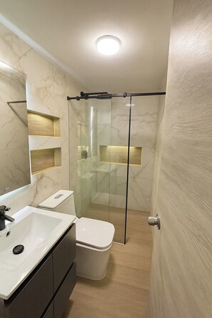 Een moderne badkamer met een douchecabine van glas, een witte wastafel en een toilet.