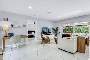 A modern living room with a flat-screen TV, a sofa, a desk with a chair, and a coffee table. - Villa Capucine Beach Retreat | Pool | Games (Pompano Beach)