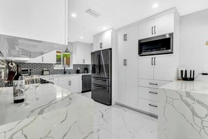 A modern kitchen with white cabinetry, a stainless steel refrigerator, and a built-in microwave. - Villa Capucine Beach Retreat | Pool | Games (Pompano Beach)