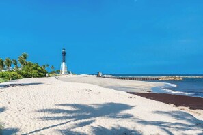 Ein Strand mit einem Leuchtturm, blauem Himmel und ruhiger See.