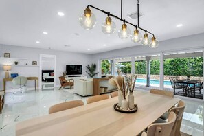 A modern living room with a large dining table, a TV, and a pool view. - Villa Capucine Beach Retreat | Pool | Games (Pompano Beach)