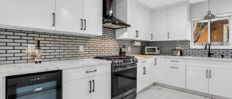 A modern kitchen with white cabinetry, a black stove, and a brick backsplash.
