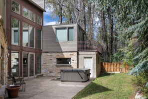 A modern two-story house with a stone facade, a patio with outdoor furniture, and a hot tub. - Booth Creek Lodge | 4BR East Vail Retreat, Sleeps 8 (Vail)