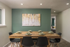 A dining area with a wooden table set for six, surrounded by black chairs. A large abstract painting adorns the green wall above the table. - Hot Tub, Sauna, Fire Pit, Huge Yard near Denver and Red Rocks (Arvada)