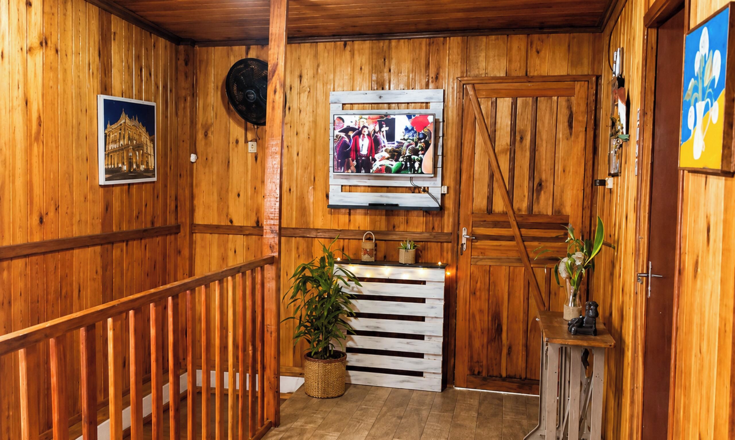 Interior de madeira com escada de madeira, televisão na parede e porta com puxador decorativo.
