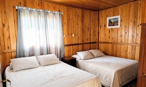 Una habitación con dos camas, paredes de madera, una ventana con cortinas, una mesita de noche y un cuadro en la pared.