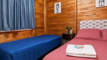 A room with two beds, wooden walls, a window with curtains, and two framed pictures.