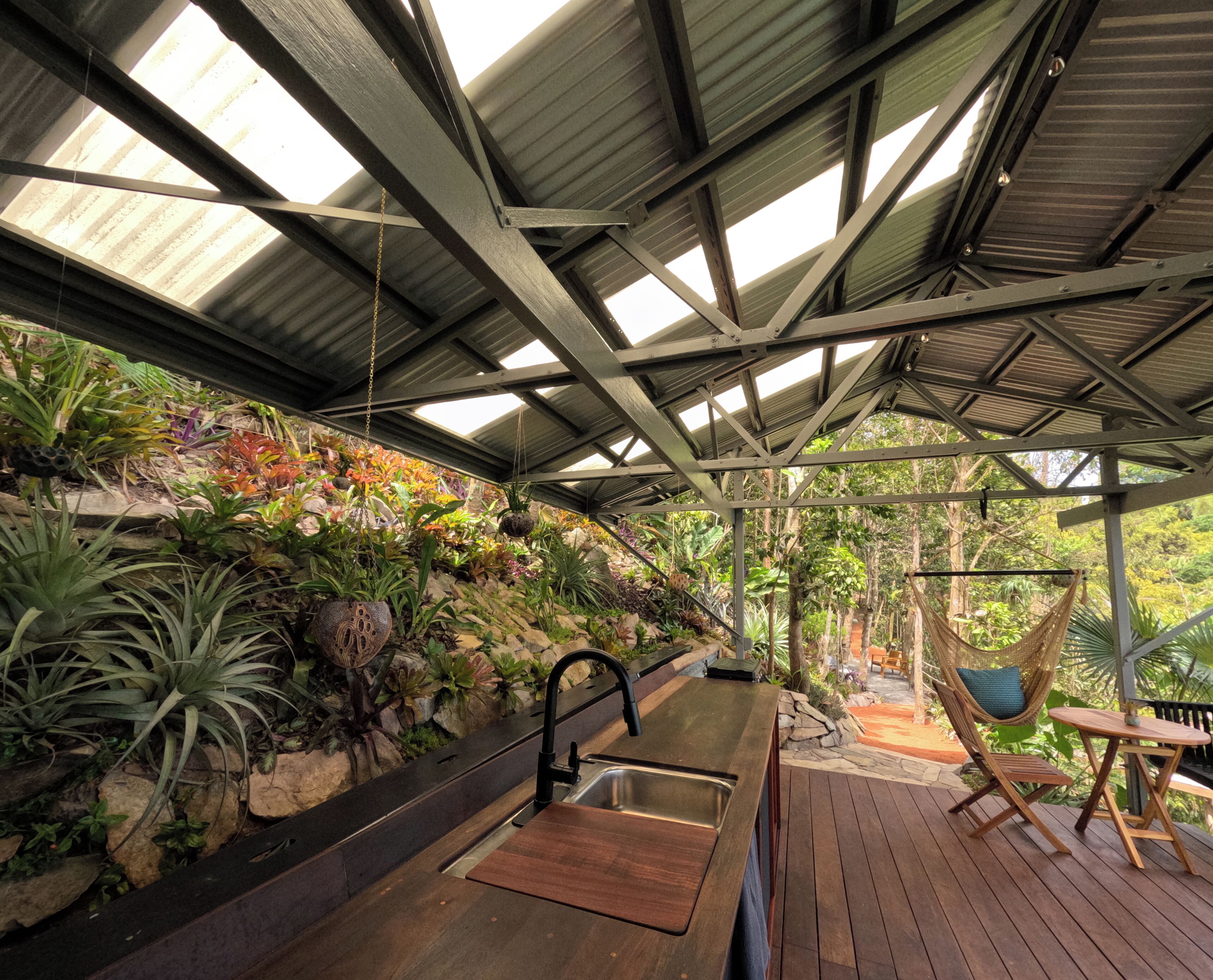 Un espace extérieur abrité, doté d’une terrasse en bois, d’un fauteuil suspendu et de diverses plantes.