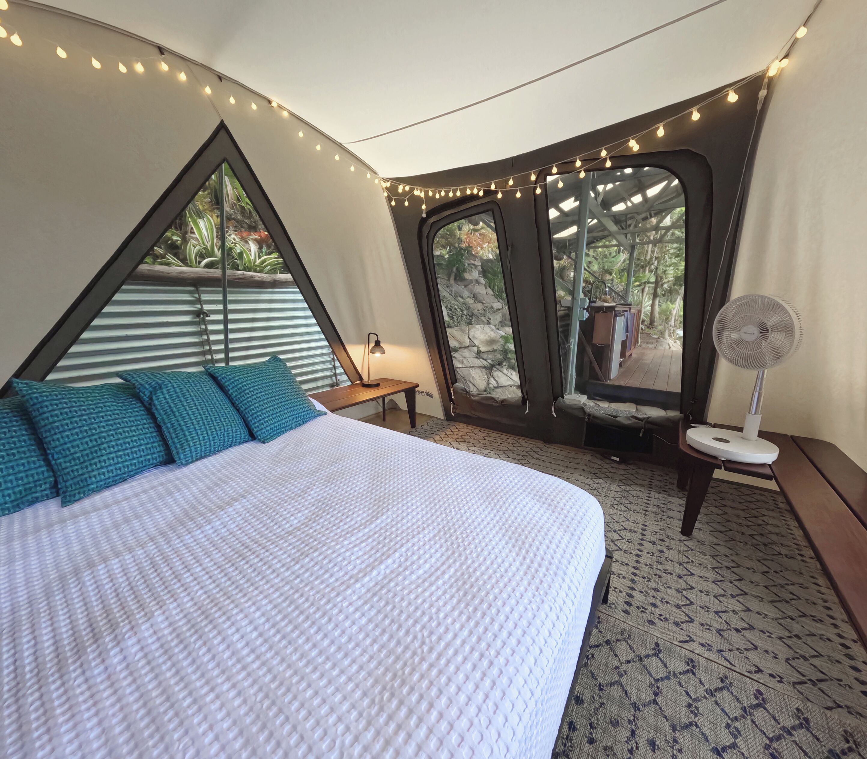 A bedroom with a bed, pillows, a fan, and a view of the outdoors.