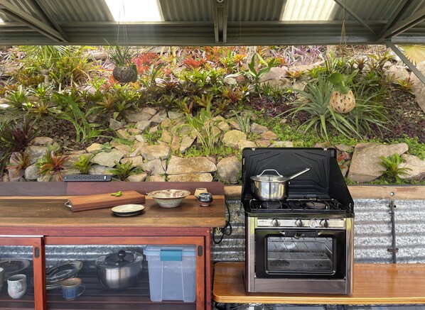 An outdoor cooking area with a gas stove and oven, surrounded by a variety of plants and rocks.