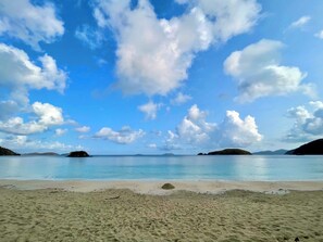 A beach with clear skies and calm water, surrounded by small islands.