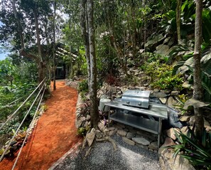 A covered outdoor area with a barbecue grill, surrounded by rocks and greenery.