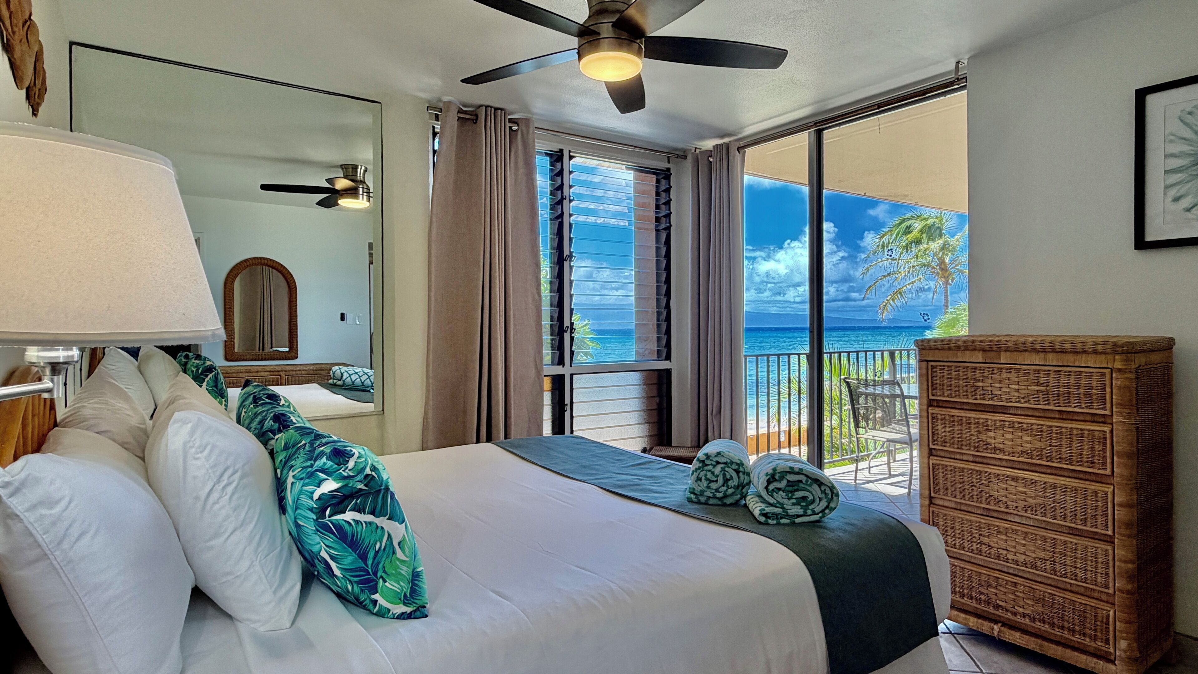 Ein Hotelzimmer mit Bett, Deckenventilator, großem Fenster mit Meerblick und Holzschrank.