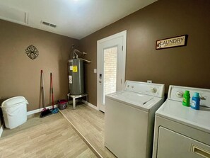 A laundry room with a water heater, washing machines, and a trash can.