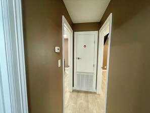 A hallway with brown walls, a white door with a red sticker, and a vent on the floor.