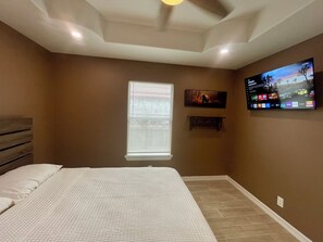 A bedroom with a bed, a TV mounted on the wall, and a window with blinds.