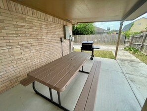 Een overdekt terras met een picknicktafel en een barbecue.