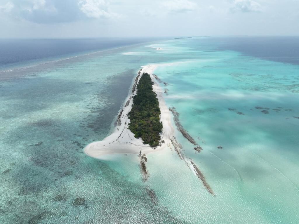 Vista aérea de una isla estrecha y alargada con un banco de arena central rodeado de aguas turquesas cristalinas.