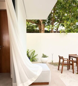 A modern outdoor seating area with a white cushioned bench, wooden chairs, and potted plants. - Chic 6-bedroom Chalet in Goidhoo, Baa Attol (Goidhoo)