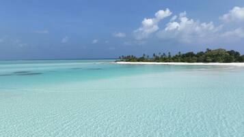 Ein klares türkisblaues Meer mit einem Sandstrand und einer kleinen Insel mit Bäumen in der Ferne.