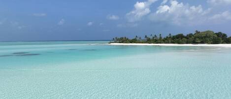 A clear turquoise sea with a sandy beach and a small island with trees in the distance.