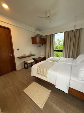 A bedroom with a bed, a desk, a chair, a window with curtains, and a ceiling fan.