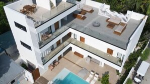 Ein modernes Mehrfamilienhaus mit Pool auf dem Dach, Außenbereich mit Sitzgelegenheiten und üppiger Bepflanzung rund um das Anwesen.