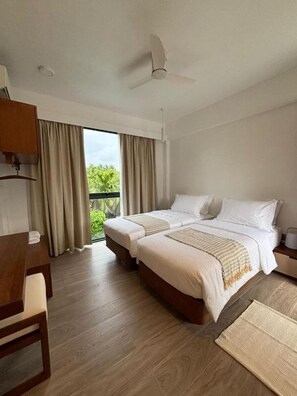A hotel room with two beds, a desk, a chair, a ceiling fan, and a view of greenery outside. - Chic 6-bedroom Chalet in Goidhoo, Baa Attol (Goidhoo)