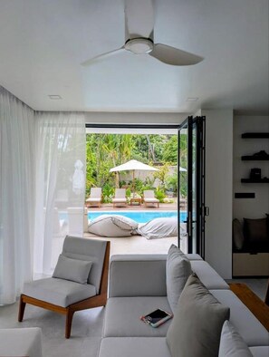 Un salon moderne avec un canapé, des fauteuils et une vue sur une piscine extérieure.