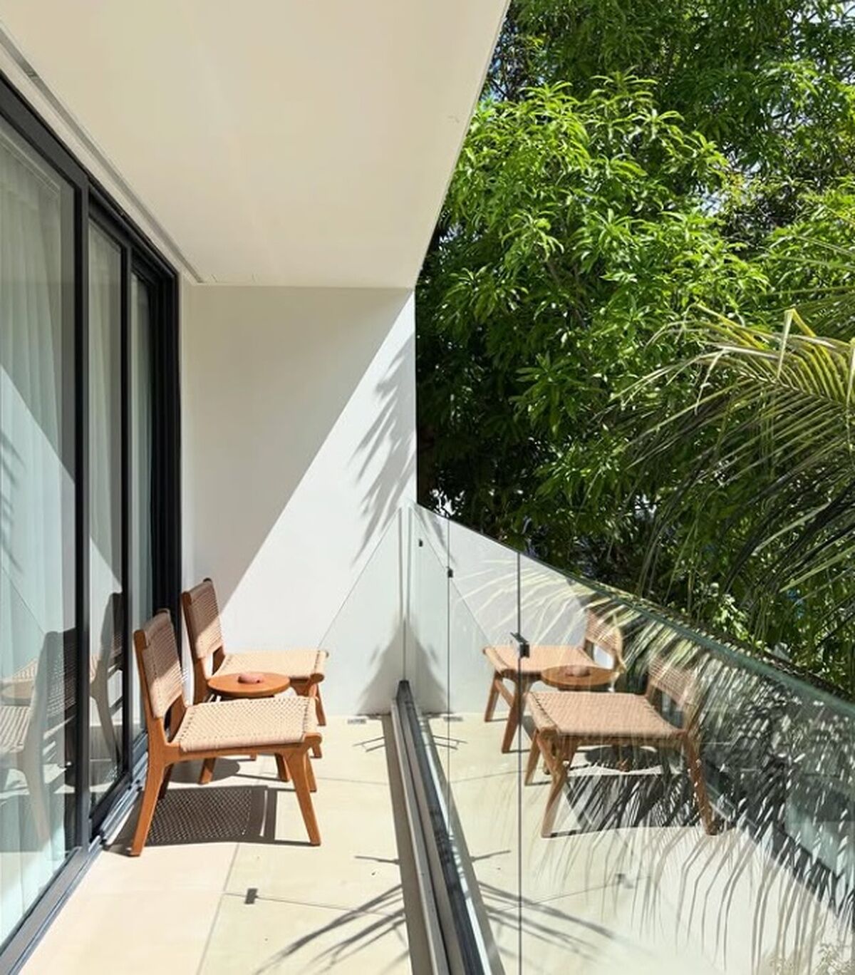 Ein Balkon mit zwei Korbstühlen und einem Glasgeländer, der auf eine üppige Grünanlage blickt.