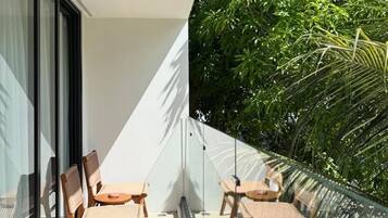 Ein Balkon mit zwei Korbstühlen und einem Glasgeländer, der auf eine üppige Grünanlage blickt.