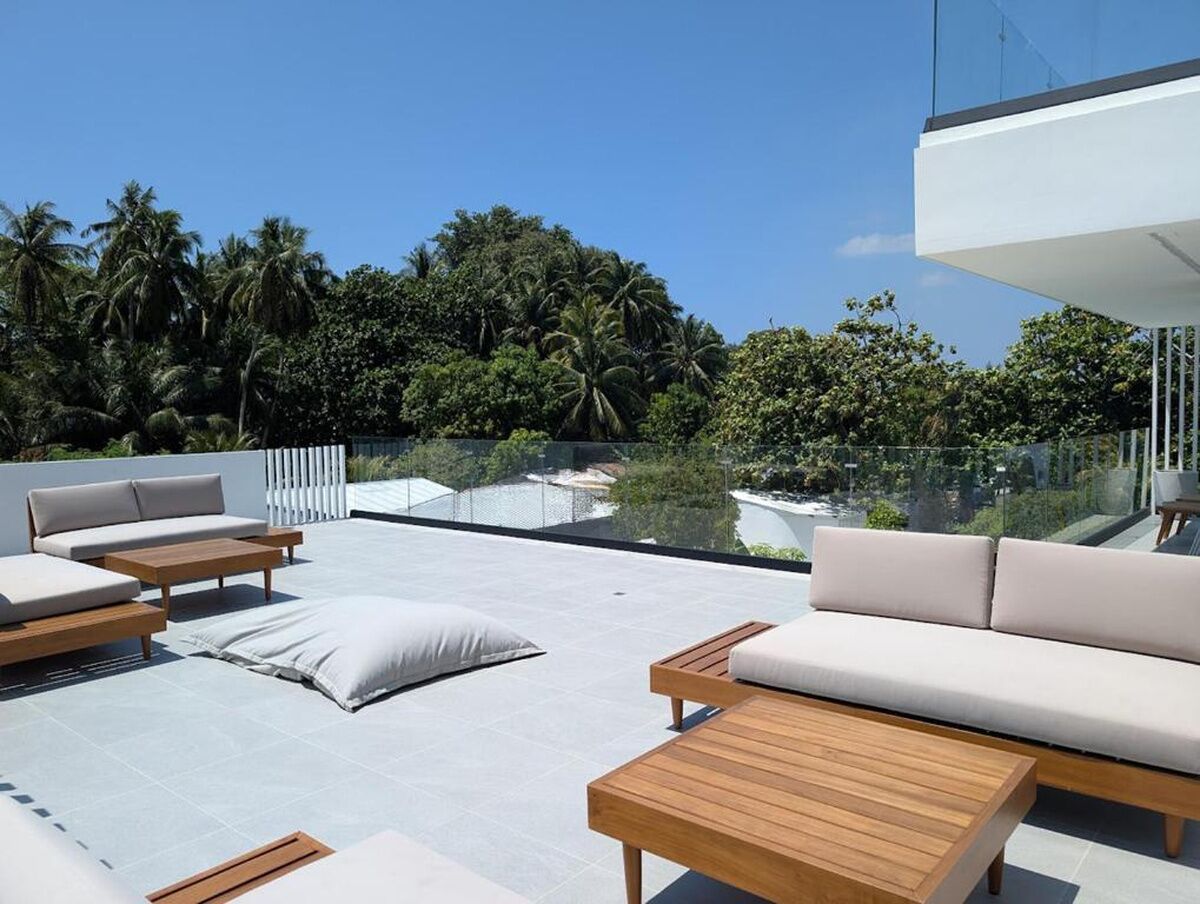 Eine Dachterrasse mit Sitzgelegenheiten im Freien, einer Glasbrüstung und Blick auf eine tropische Landschaft.